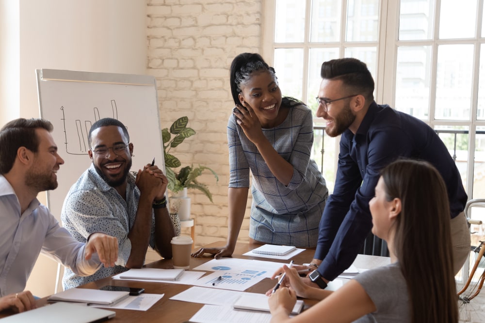 5 pessoas sorriem ao redor de uma mesa de reuniões no ambiente corporativo